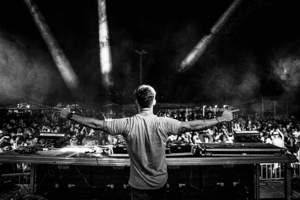 DJ on stage with arms outstretched, facing a large crowd at night
